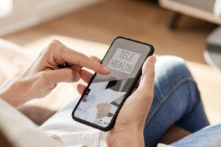 text telehealth on the screen of a smartphone closeup of a young caucasian man, sitting comfortably in a couch, using his smartphone, with the text telehealth on its screen